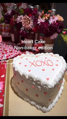 a heart shaped cake with the words xoxo on it and flowers in the background