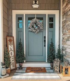 a blue front door with two christmas trees on the side and a welcome mat in front