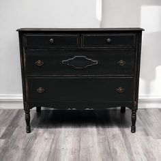 an old black dresser is sitting on the floor in front of a white wall and wooden floors