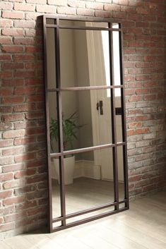 an empty room with a brick wall and large mirror on the floor next to a potted plant