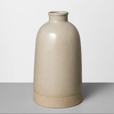 a white vase sitting on top of a table next to a gray wall and floor