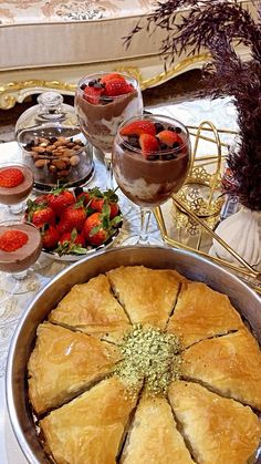 a table topped with pies and desserts next to wine glasses filled with strawberries