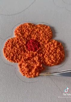 an orange crocheted flower with a red center being worked on by a needle