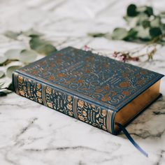 an old book sitting on top of a marble table next to some leaves and flowers