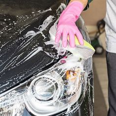 a person washing a car with a sponge and detergent on the headlight cover