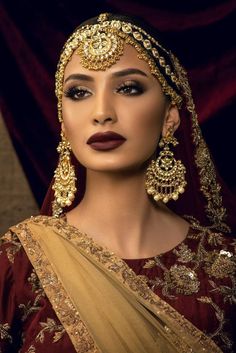 a woman in a red and gold outfit with jewelry on her head, looking at the camera