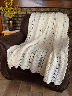 a white crocheted blanket sitting on top of a brown leather chair next to a brick wall