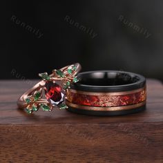 two wedding rings with red and green stones on them sitting on top of a wooden table