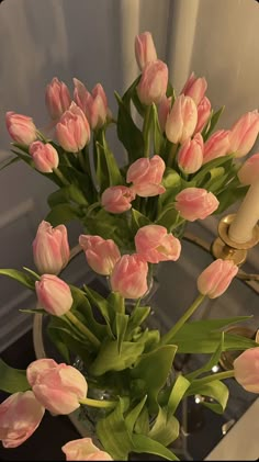 a vase filled with pink tulips sitting on top of a table next to a candle