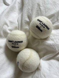 three white balls with black writing on them are laying on a bed sheet and one is in the shape of a tennis ball