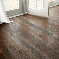 an empty room with wood flooring and white curtains on the window sill,