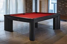 a pool table with red cloth on it in front of a brick wall and windows