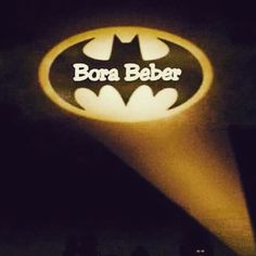 the batman logo is lit up in front of some buildings at night, and it says bora beber