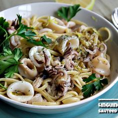 a white bowl filled with pasta covered in mushrooms and parsley next to a lemon wedge