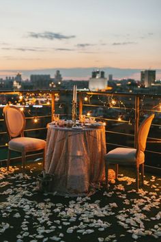 a table set up with candles and flowers on top of a roof overlooking the city