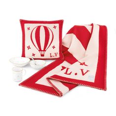 the red and white blanket is next to two teacups, one with a hot air balloon on it