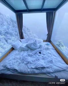 an unmade bed sitting in front of a window on top of a snow covered mountain