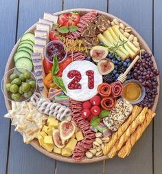 a platter filled with cheese, crackers, fruit and other foods on top of a wooden table