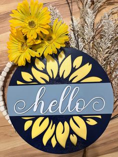 a blue and yellow sign that says hello with daisies in front of some dried flowers