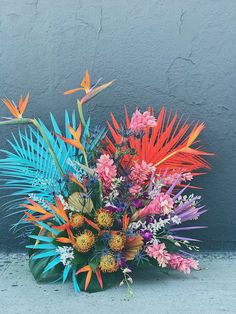 a vase filled with lots of colorful flowers on top of a cement floor next to a wall