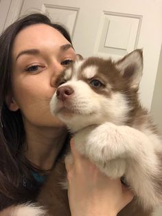 a woman holding a husky puppy in her arms and kissing it's face with its mouth