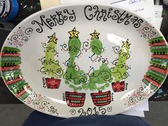 a white plate decorated with christmas trees and potted plants on the bottom, says merry christmas