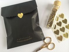 a pair of scissors next to a black bag with gold hearts on it and some confetti