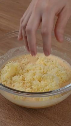 someone is adding cheese to a dish in a glass bowl on a wooden countertop