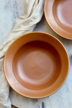 two brown plates sitting on top of a marble counter next to an orange plate and napkin