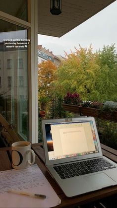 an open laptop computer sitting on top of a wooden table next to a cup of coffee