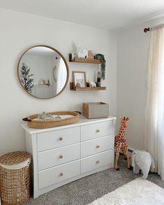 a baby's room with a dresser, mirror and toy giraffe