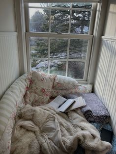 an unmade bed sitting in front of a window with a book on top of it