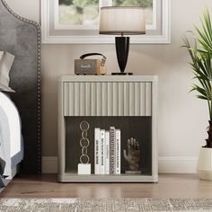 a nightstand with books and a lamp on top of it in front of a window