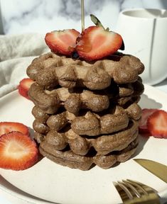 a stack of chocolate waffles topped with strawberries on a plate next to a fork