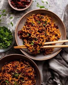 two bowls filled with noodles and chopsticks on top of a gray tablecloth