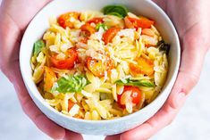 two hands holding a bowl of pasta with tomatoes and basil on top, while another hand holds the bowl