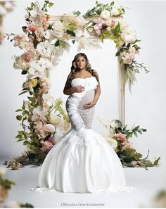 a pregnant woman in a white gown standing under a floral arch with flowers on it