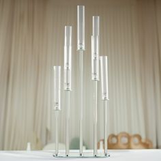 four clear glass candlesticks sitting on a white table with curtains in the background