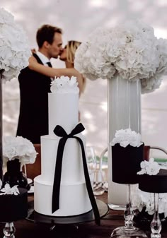 a bride and groom kissing in front of their wedding cake at the reception table with white flowers