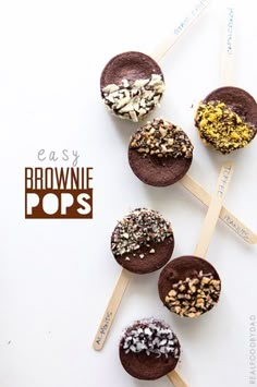 four chocolate brownie pops with sprinkles and nuts on top, sitting on wooden sticks