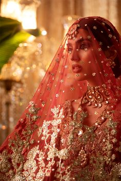 a woman wearing a red and gold bridal veil in front of a chandelier