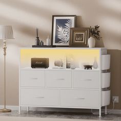 a white dresser sitting in a living room next to a lamp and pictures on the wall