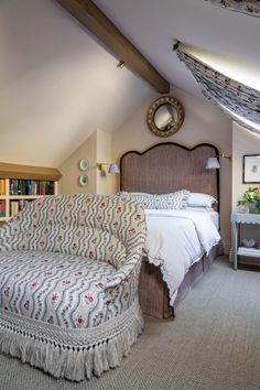 a bed sitting under a window next to a chair and book shelf on top of a carpeted floor