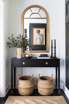 a black console table with two baskets underneath it and a mirror on the wall behind it