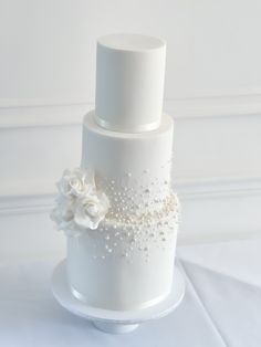 a three tiered wedding cake with white flowers and pearls on the top, sitting on a table