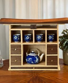 a wooden cabinet with blue and white dishes in it on a table next to a potted plant