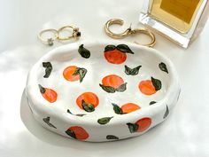 a white bowl with oranges painted on it next to a keychain and perfume bottle