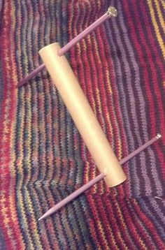 a piece of wood sitting on top of a colorful blanket next to a pair of knitting needles