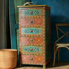 an ornately painted chest of drawers next to a wicker basket on the floor