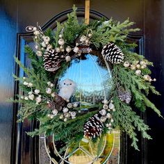 a wreath is hanging on the front door with pine cones and other holiday decorations around it